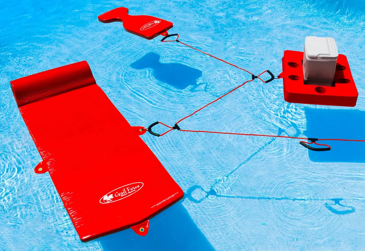 Red floating pool lounge and cooler, connected by ropes, common for summer relaxation and pool parties, showcasing vibrant colors against blue water.