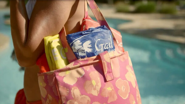 A colorful beach bag, featuring a blue towel with palm tree designs, is slung over a shoulder near a pool, emphasizing summer leisure.
